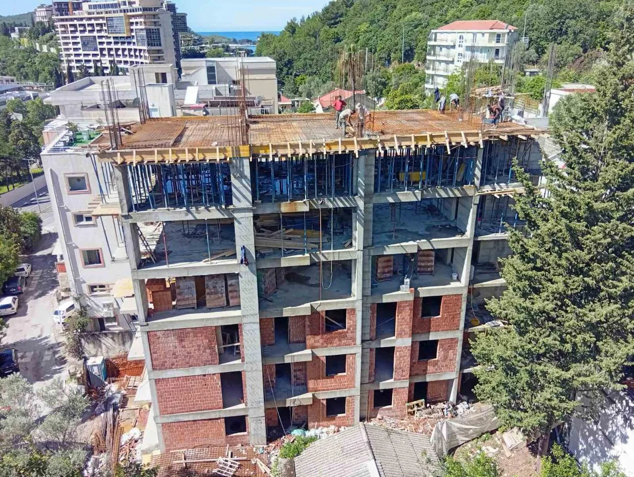 Reinforced concrete frame of a residential building under construction in Bečići, Budva, with the Adriatic visible behind it.
